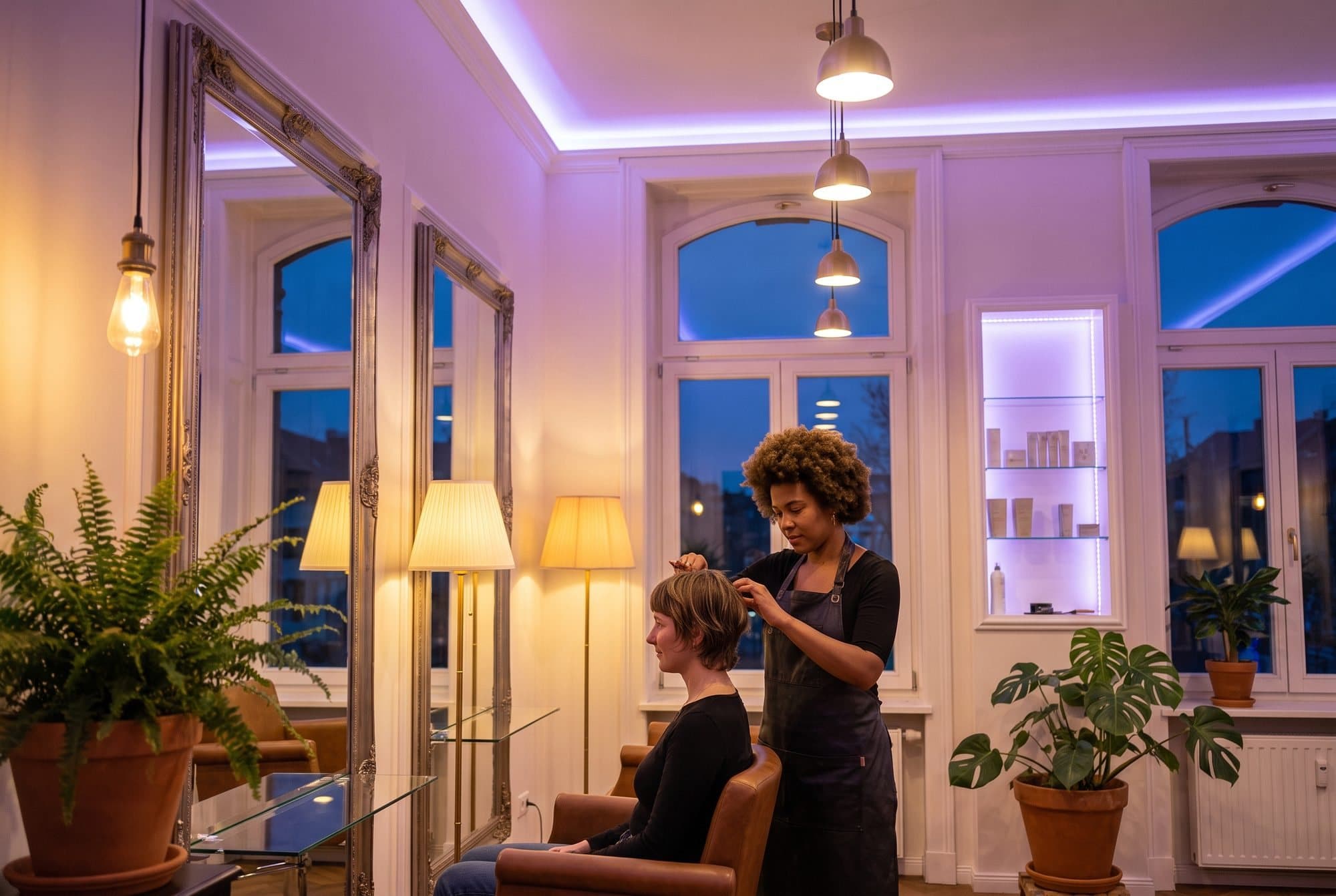 Friziere ķemmē klientes matus gaišā salonā ar augiem